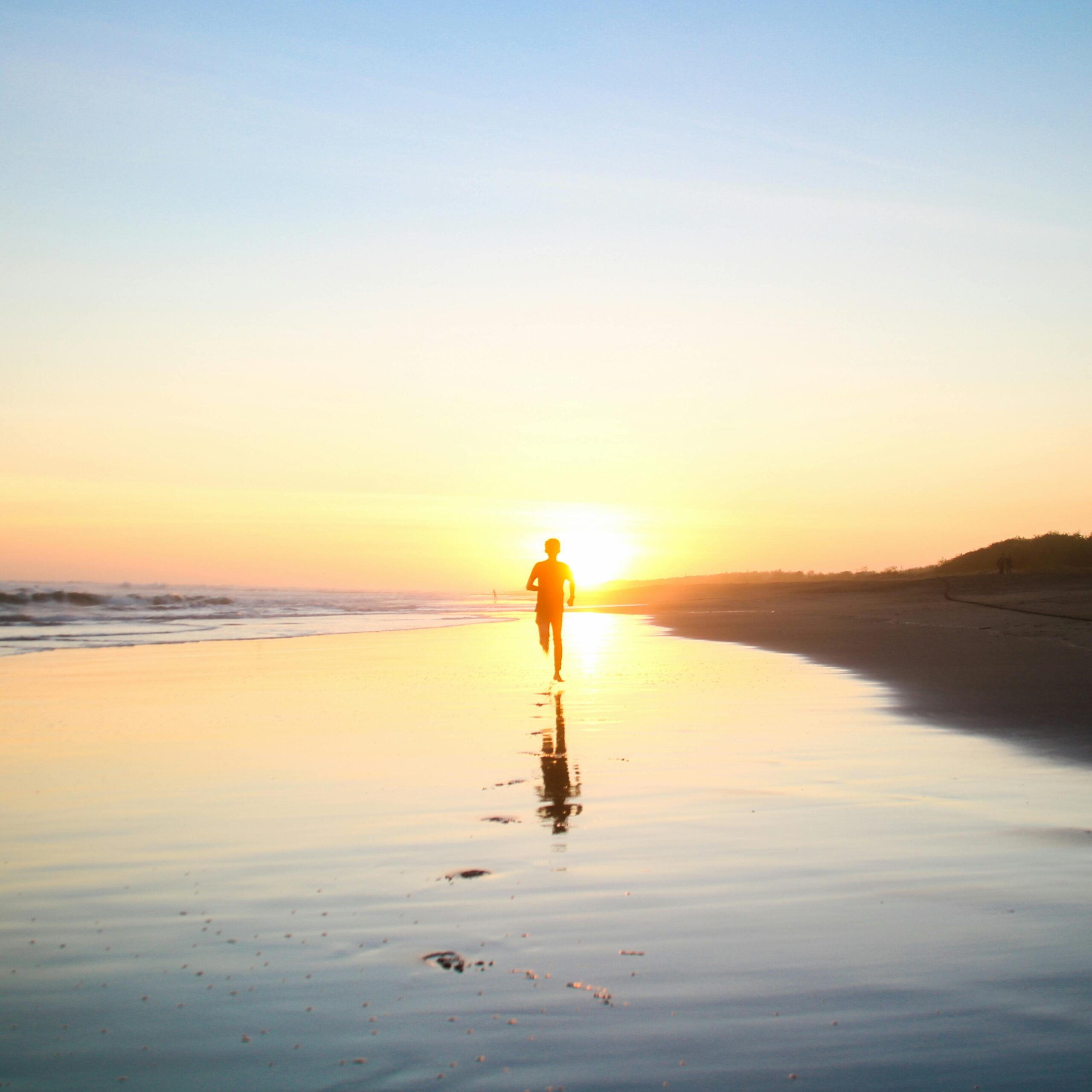 Person der løber på stranden mod en smuk solopgang med havet til venstre og strandens sand til højre.